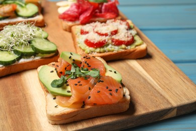 Tasty toasts with different toppings served on wooden board, closeup