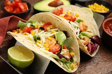 Delicious tacos with shrimps, cheese and lime on wooden table, closeup