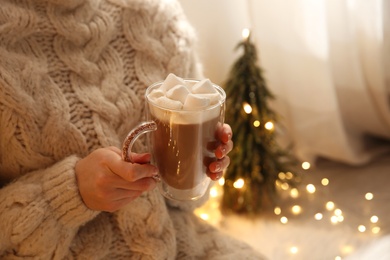 Woman holding cup of hot drink with marshmallow indoors, closeup