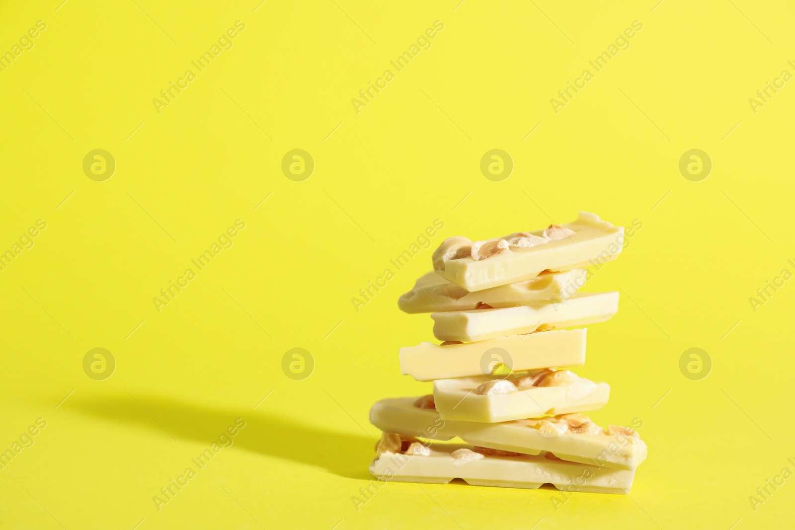 Photo of Stack of delicious white chocolate pieces with hazelnuts on yellow background, space for text