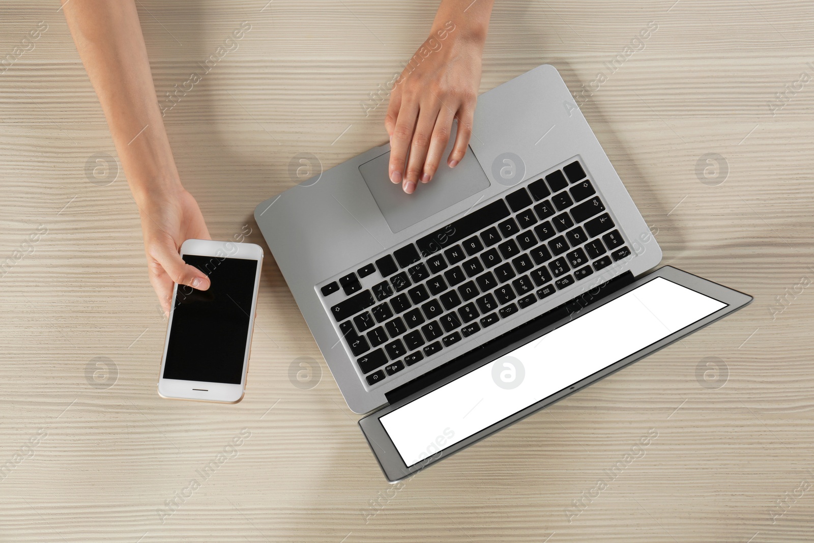 Photo of Young woman with mobile phone using laptop at wooden table, top view