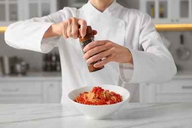 Photo of Professional chef adding pepper into delicious dish at white marble table indoors, closeup