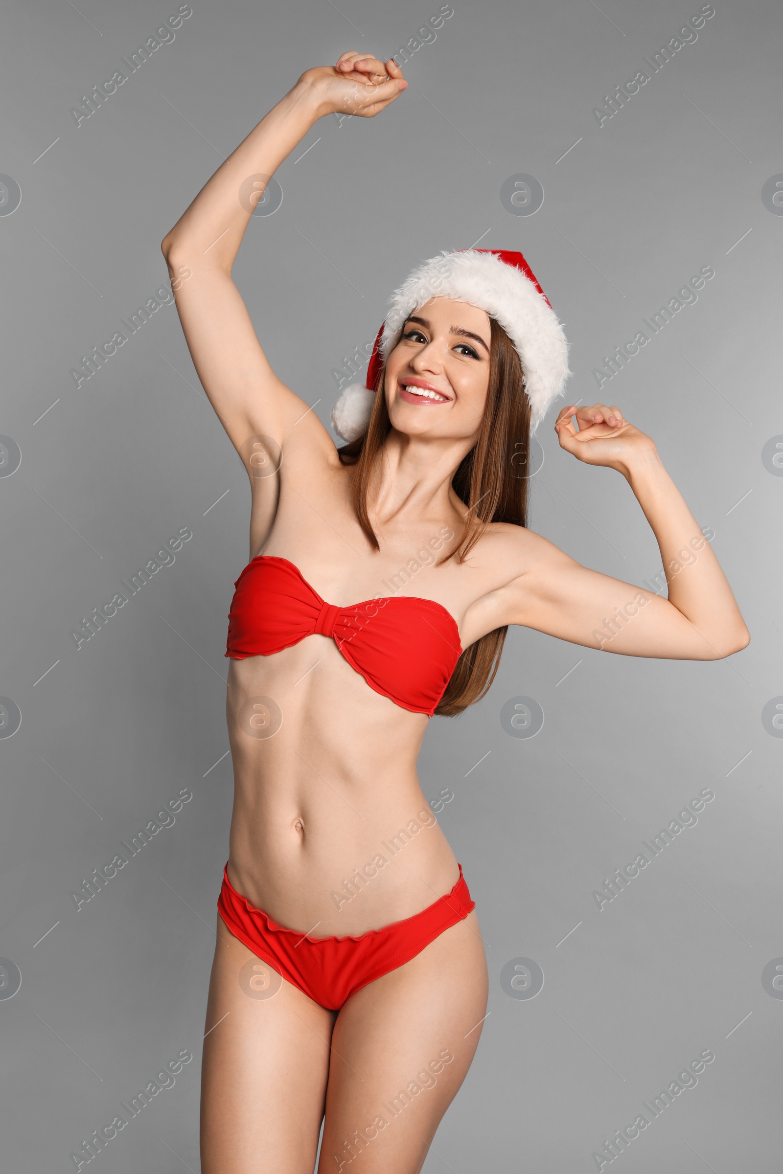 Photo of Happy young woman in red bikini and Santa hat on light grey background. Christmas celebration