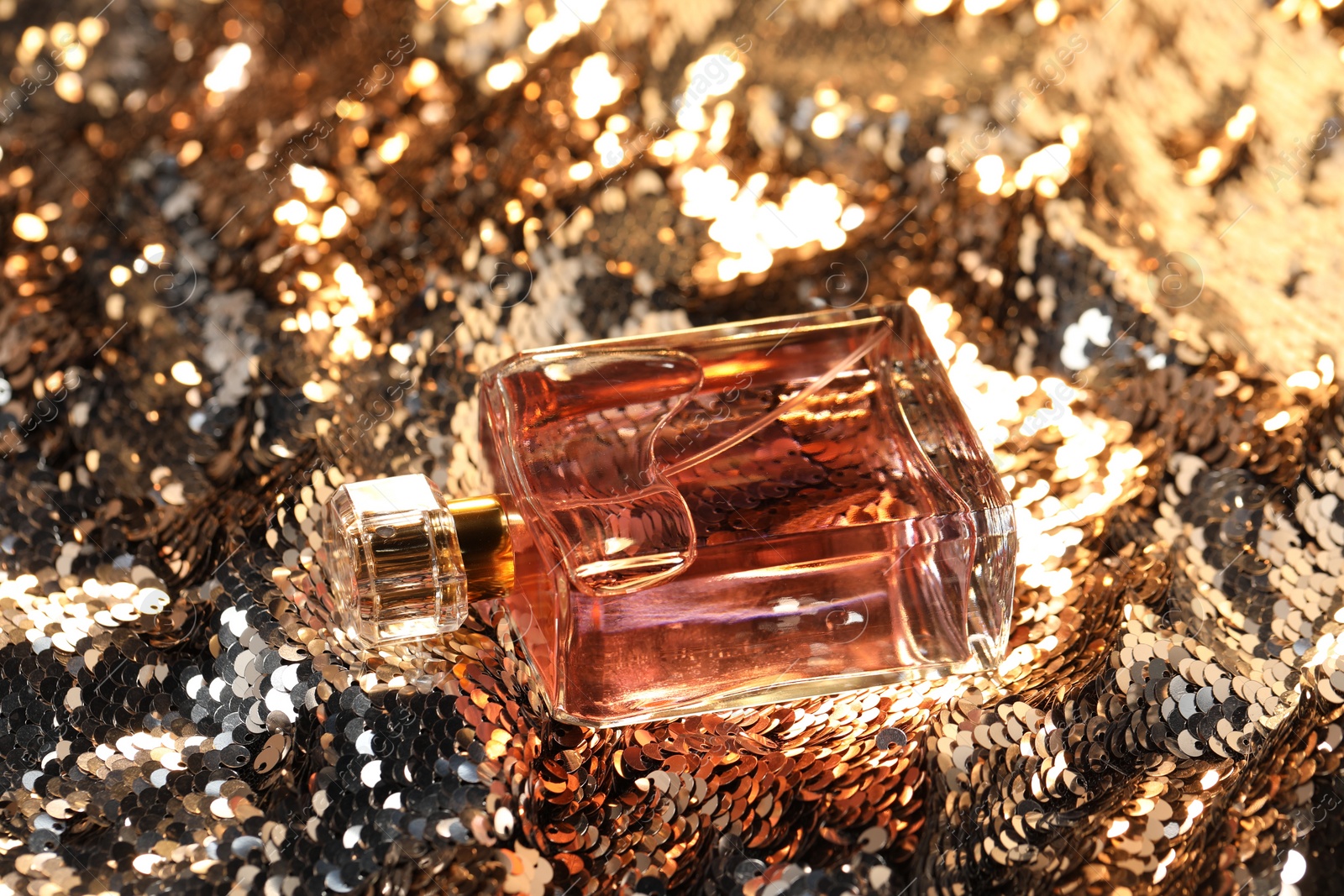 Photo of Luxury perfume in bottle on fabric with shiny sequins, closeup