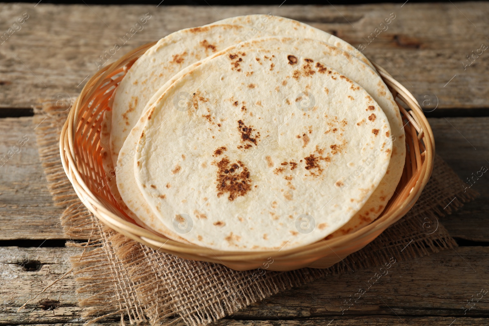 Photo of Tasty homemade tortillas in wicker basket on wooden table