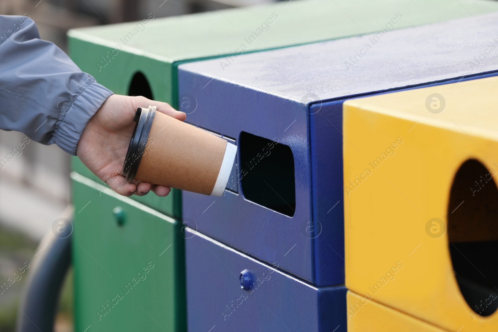 Photo of Man throwing paper coffee cup into garbage bin outdoors, closeup. Waste sorting