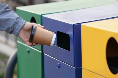 Photo of Man throwing paper coffee cup into garbage bin outdoors, closeup. Waste sorting