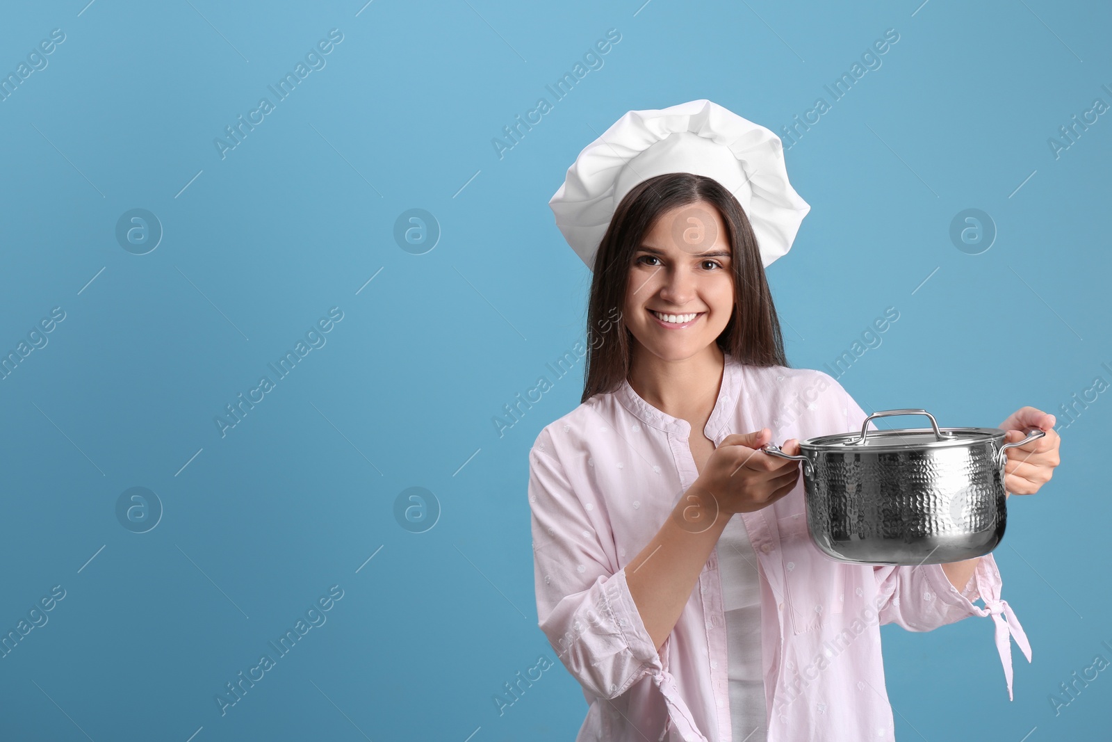 Photo of Happy young woman with cooking pot on light blue background. Space for text