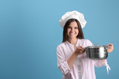 Photo of Happy young woman with cooking pot on light blue background. Space for text