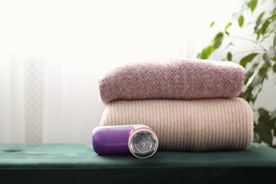 Modern fabric shaver and woolen sweaters on green bench indoors, space for text