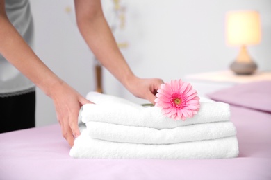 Photo of Young maid putting flower on stack of towels in hotel room