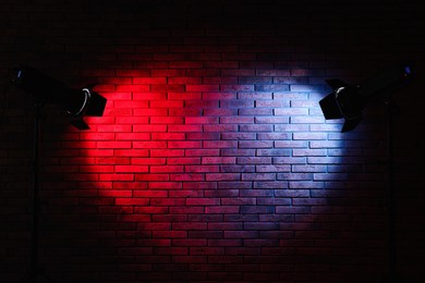 Photo of Bright blue and red spotlights near brick wall in dark room, space for text