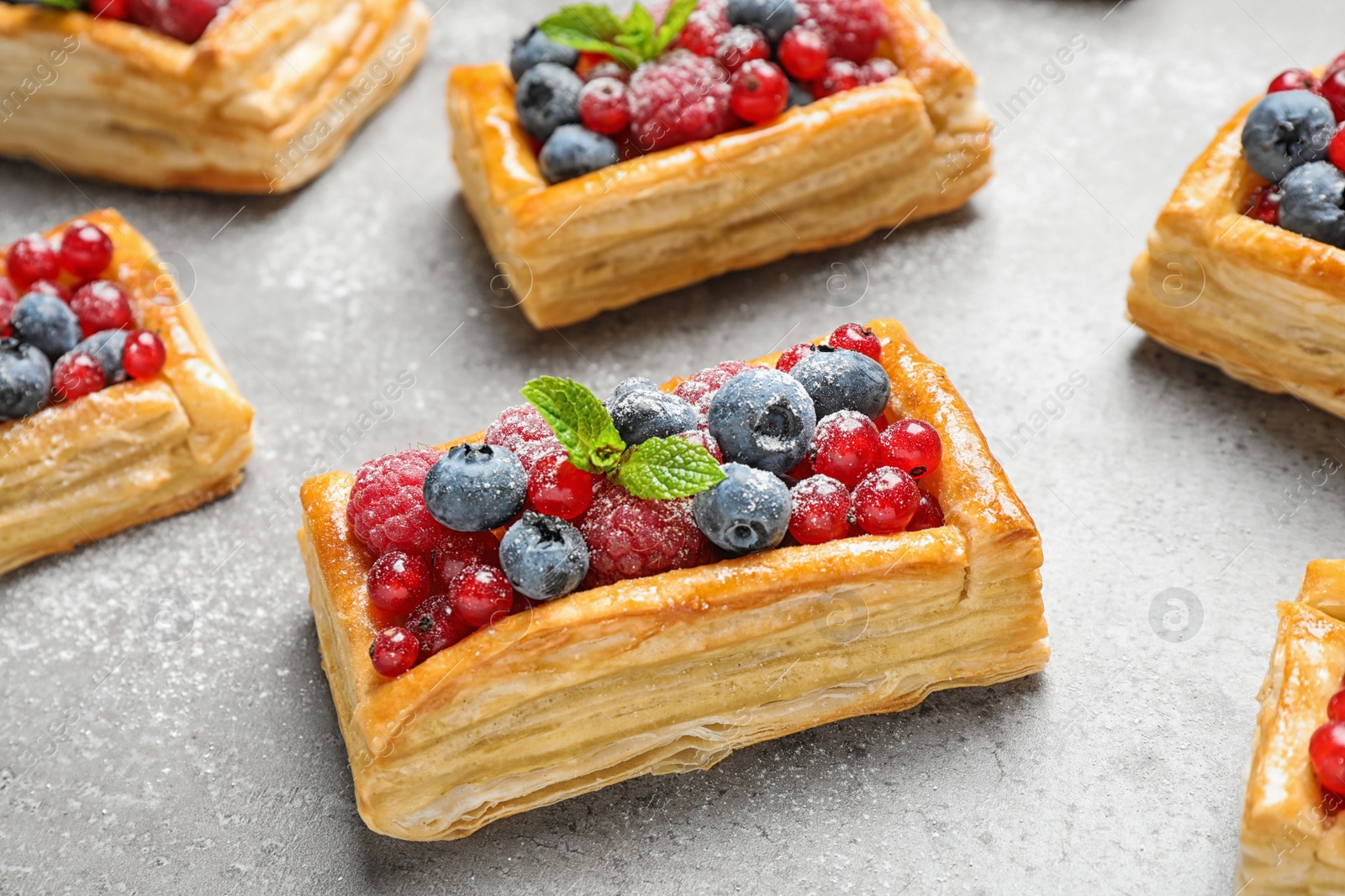 Photo of Fresh delicious puff pastry with sweet berries on grey table