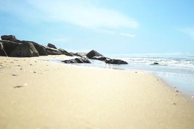 Sandy beach with rocks near sea on sunny day, closeup