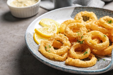 Photo of Plate with homemade crunchy fried onion rings and lemon slices on table, closeup