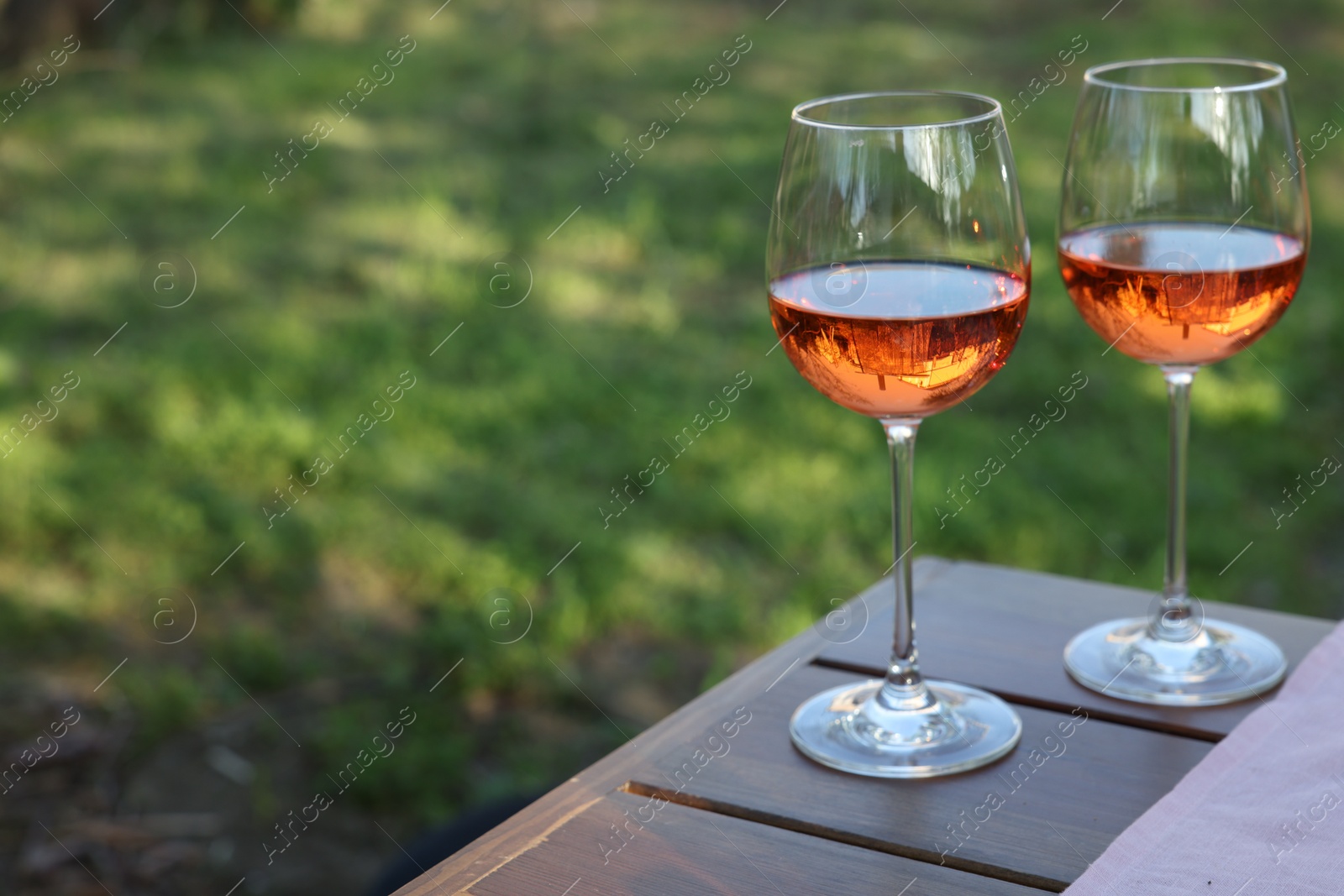 Photo of Glasses of rose wine on wooden table in garden. Space for text
