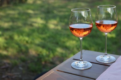 Glasses of rose wine on wooden table in garden. Space for text