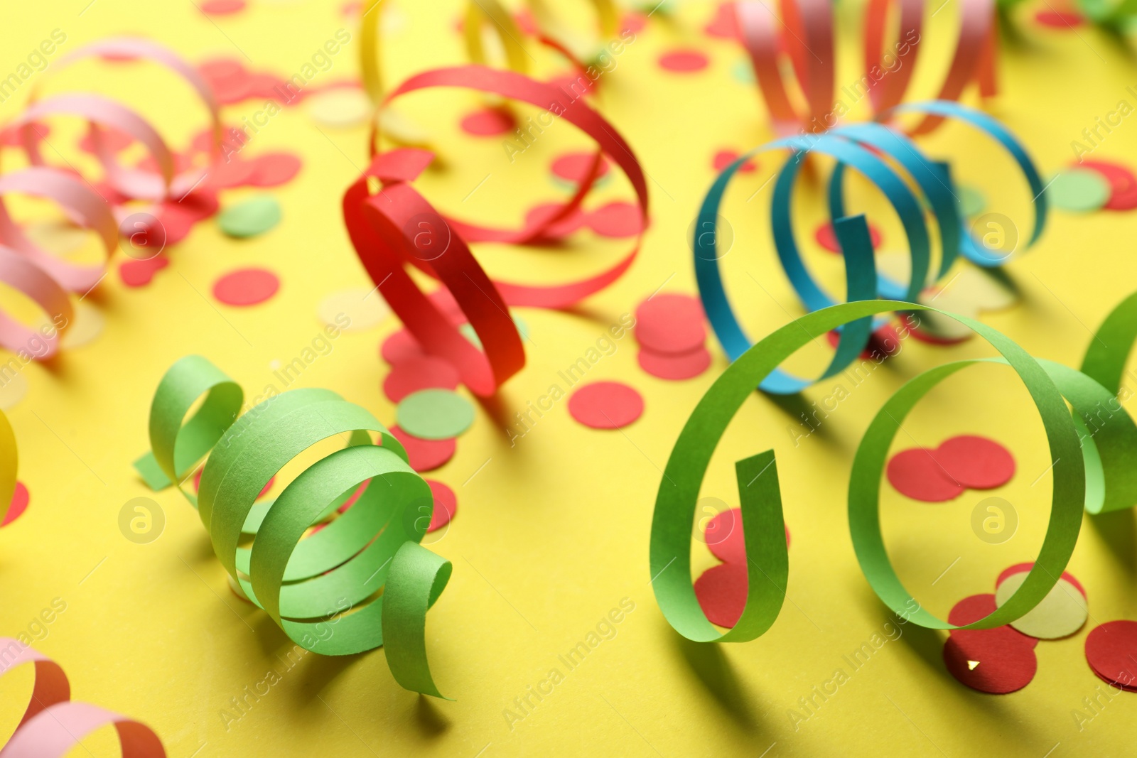 Photo of Colorful serpentine streamers and confetti on yellow background