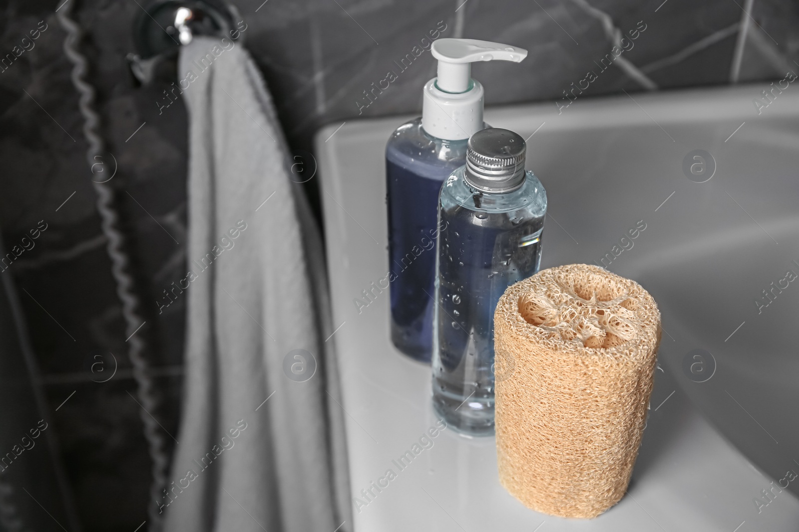 Photo of Natural loofah sponge and shower gel bottles on washbasin in bathroom. Space for text