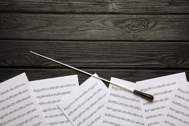 Photo of Conductor's baton and sheet music on black wooden table, flat lay. Space for text