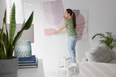 Photo of Woman on ladder hanging picture at home