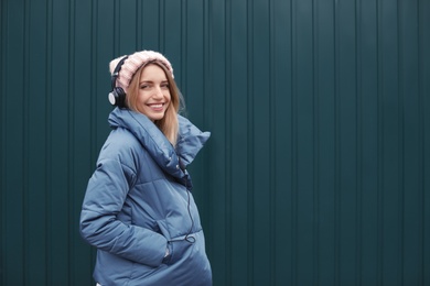 Photo of Young woman with headphones listening to music near color wall. Space for text