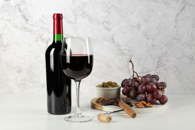 Photo of Delicious red wine, corkscrew and snacks on table against white marble background