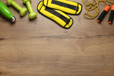 Photo of Yellow weighting agents and sport equipment on wooden table, flat lay. Space for text