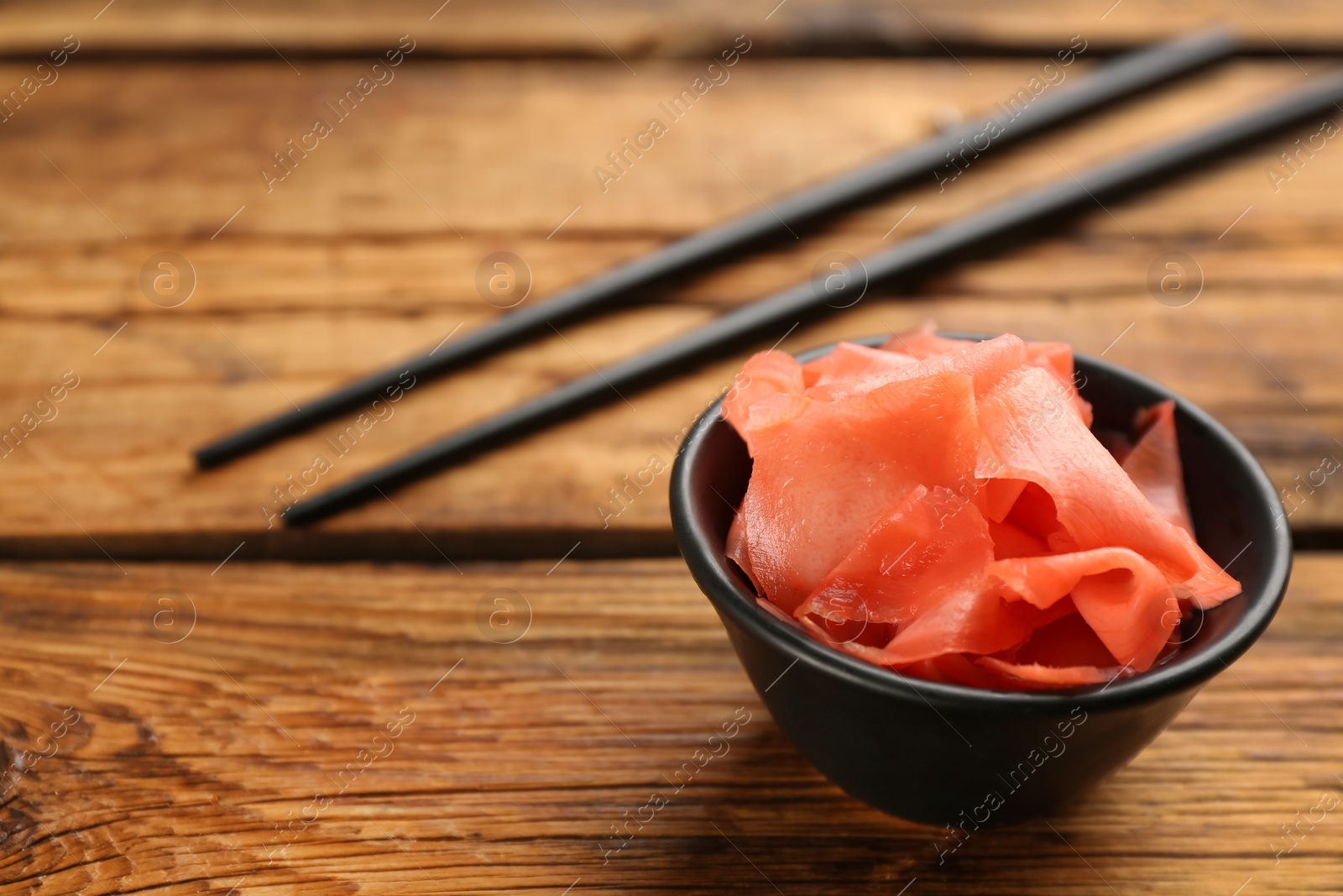 Photo of Spicy pickled ginger and chopsticks on wooden table, space for text