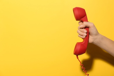 Photo of Closeup view of woman holding red corded telephone handset on yellow background, space for text. Hotline concept