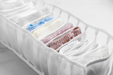 Organizer with folded women's underwear on white marble table, closeup