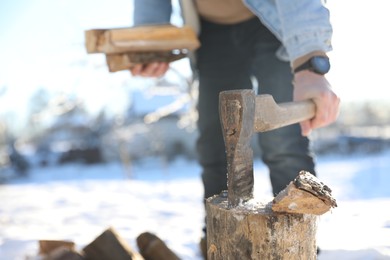 Photo of Man taking axe out of wooden log outdoors on winter day, closeup. Space for text