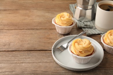 Photo of Tasty cupcakes with cream served on wooden table. Space for text