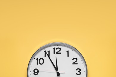 Photo of Clock showing five minutes until midnight on yellow background, top view with space for text. New Year countdown