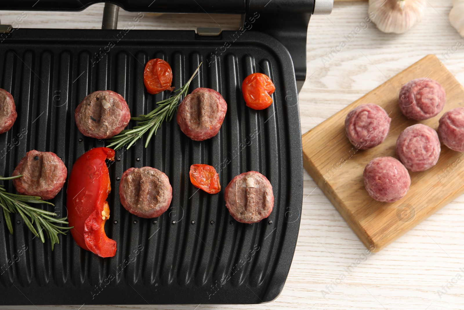 Photo of Electric grill with vegetables, meat balls and rosemary on wooden table, flat lay