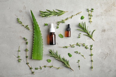 Bottles with essential oils and fresh herbs on light background, flat lay