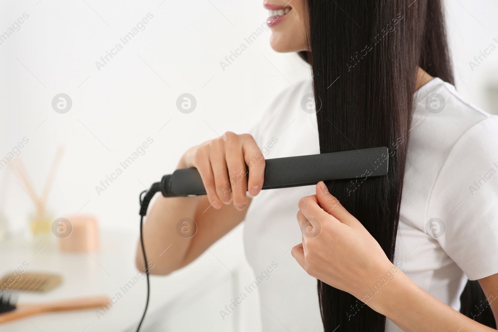 Photo of Happy woman using hair iron in room, closeup