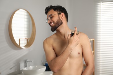 Photo of Attractive young man spraying luxury perfume indoors