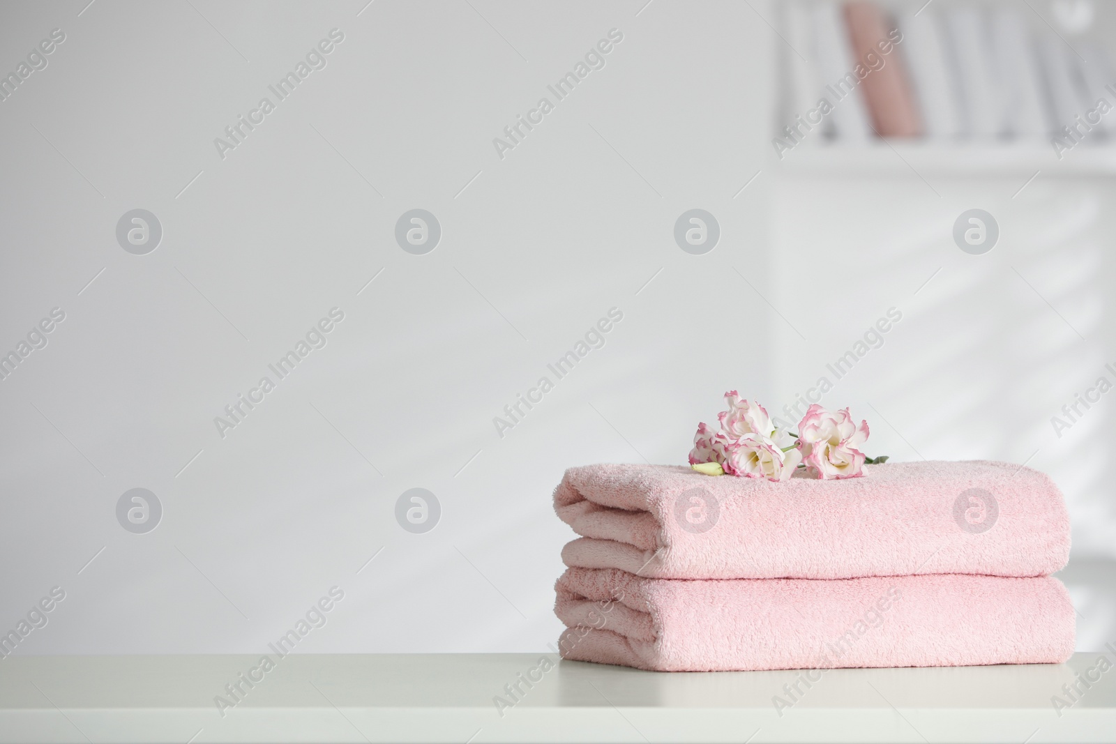 Photo of Stack of clean soft towels with eustoma flowers on white table indoors. Space for text