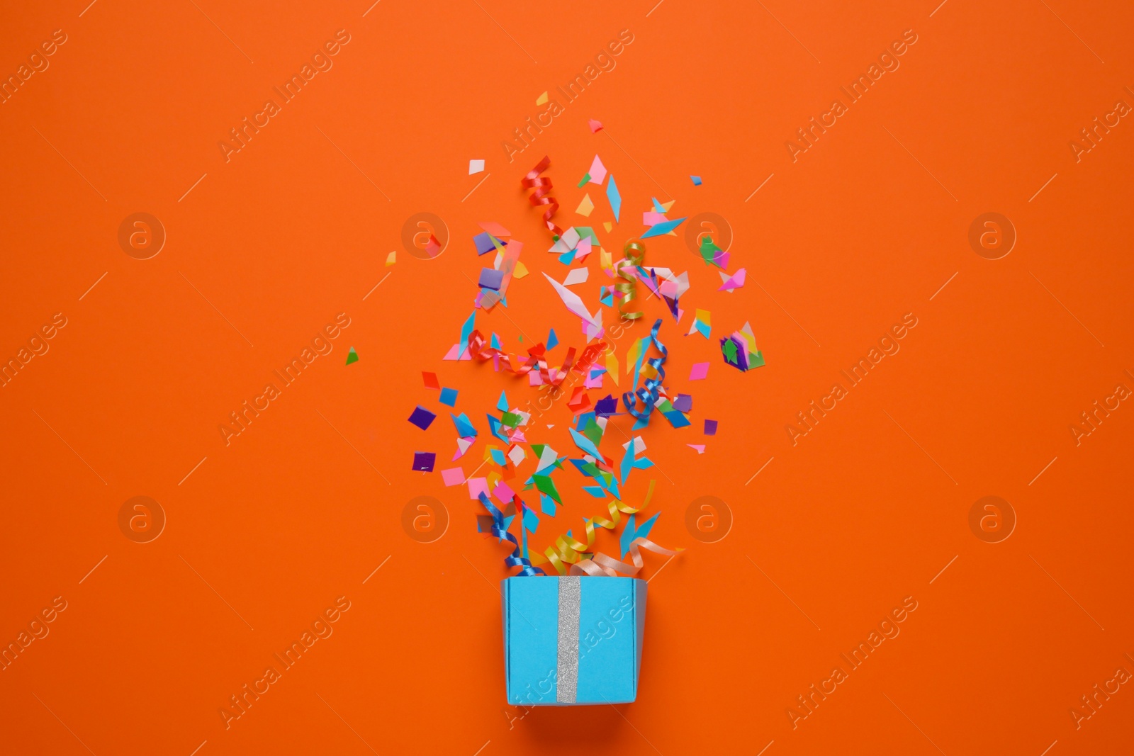 Photo of Box with bright confetti on orange background, flat lay