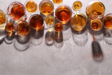 Photo of Many different liqueurs in glasses on grey textured table, flat lay. Space for text