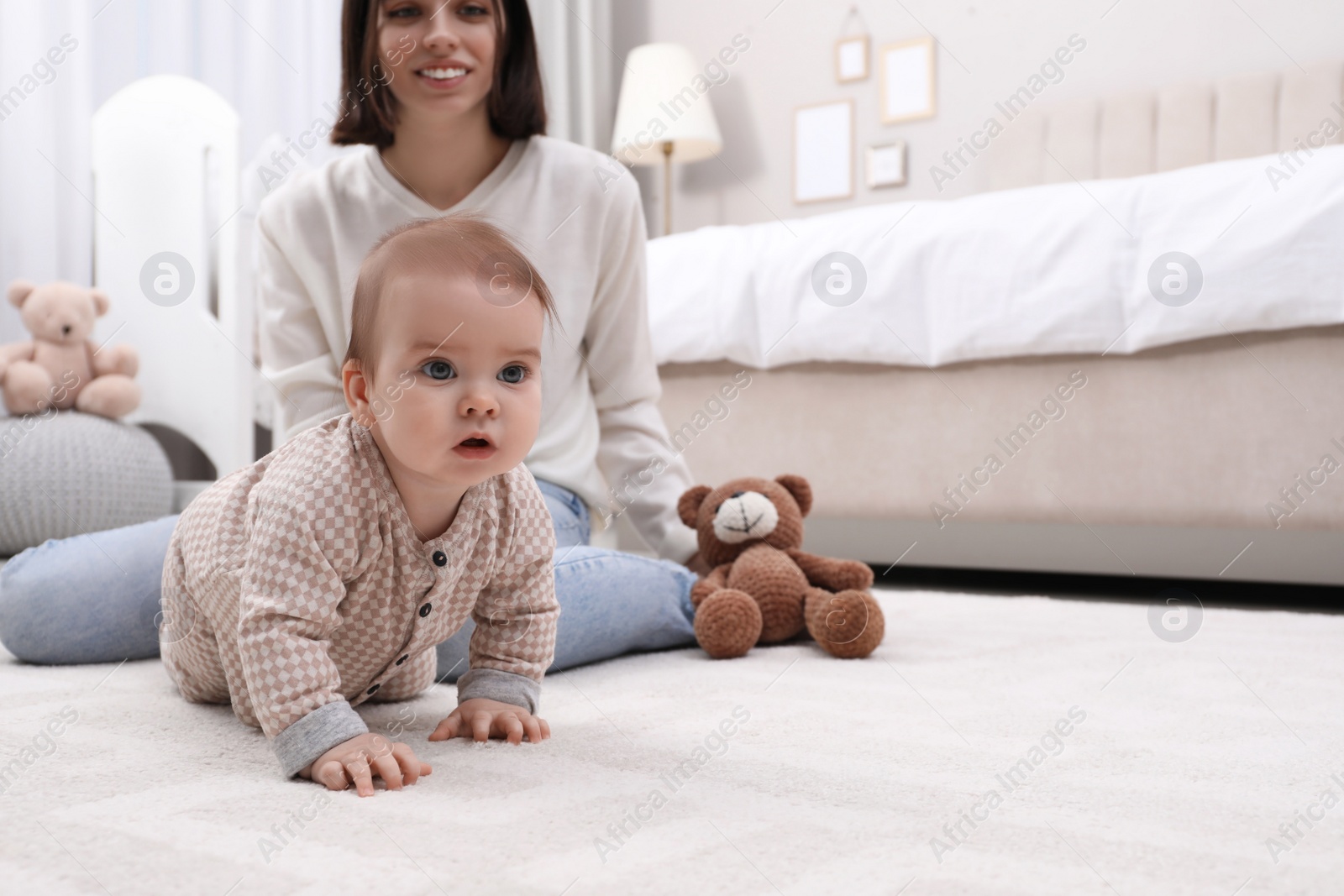 Photo of Young mother watching her cute baby crawl on floor at home