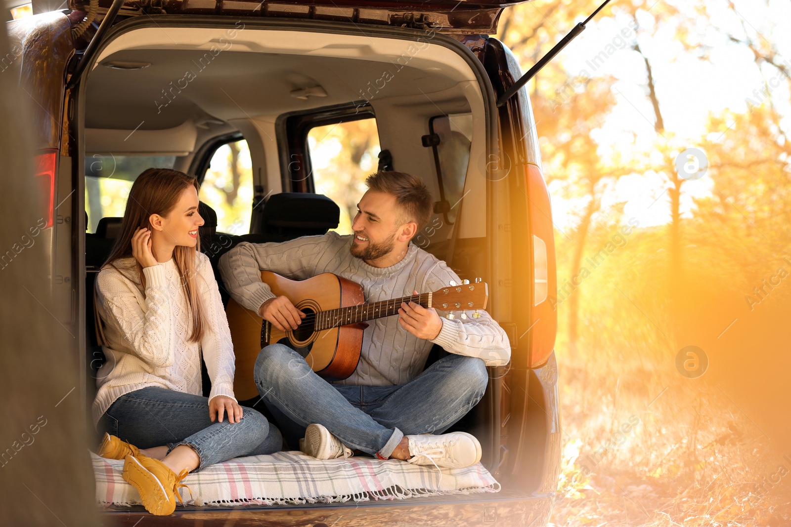 Photo of Young couple with guitar sitting in open car trunk outdoors