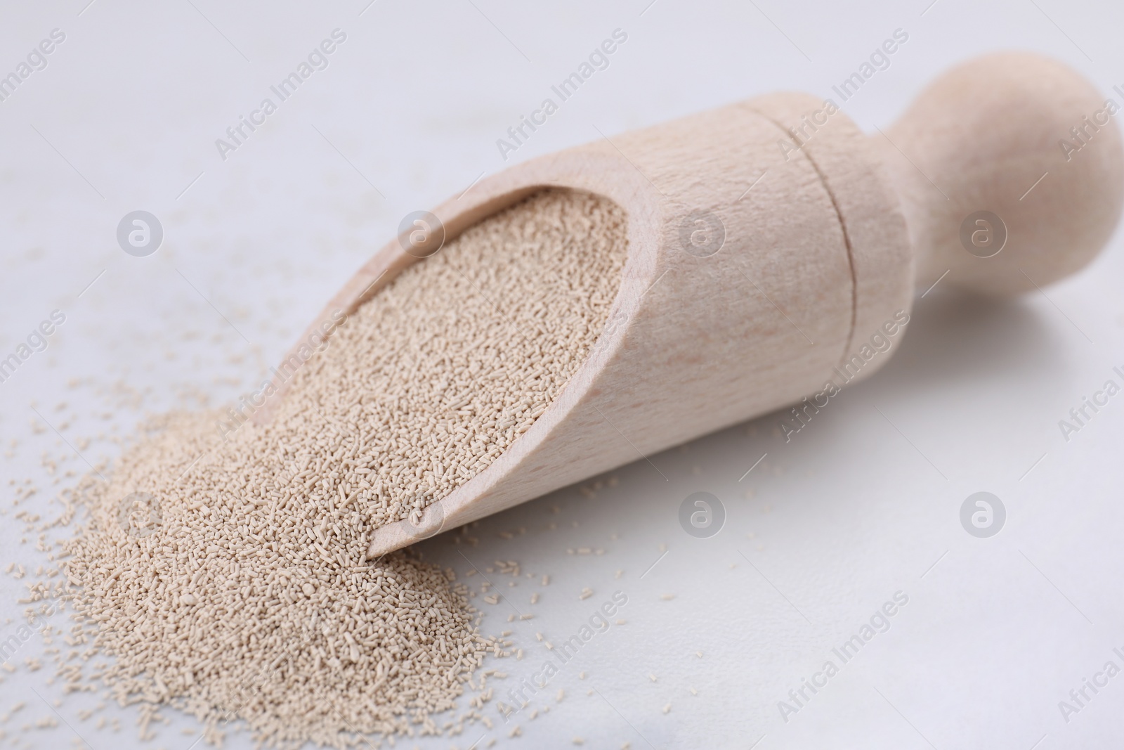 Photo of Wooden scoop with active dry yeast on white marble table, closeup