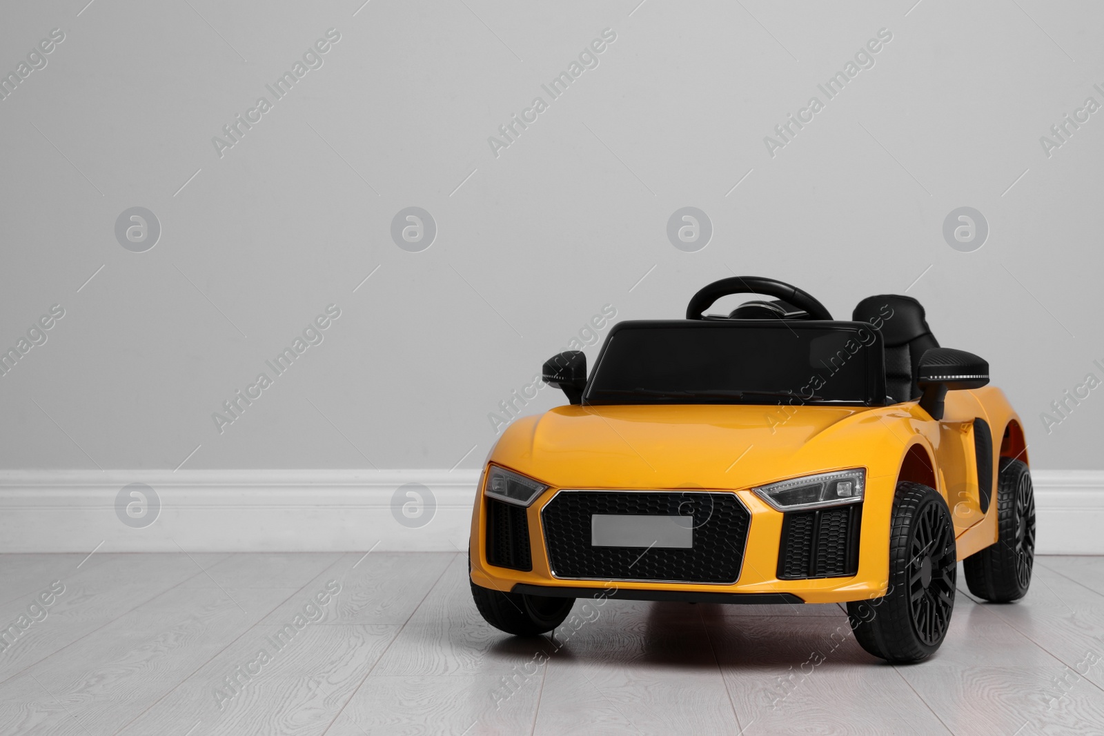 Photo of Child's electric toy car near light wall indoors. Space for text