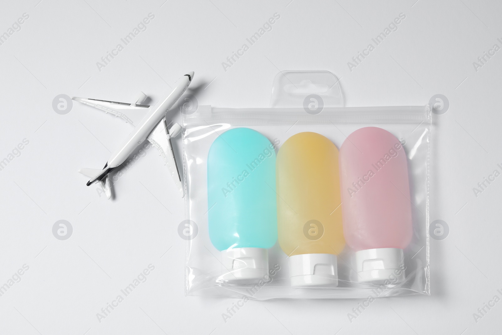 Photo of Cosmetic travel kit in plastic bag and toy plane on white background, top view. Bath accessories