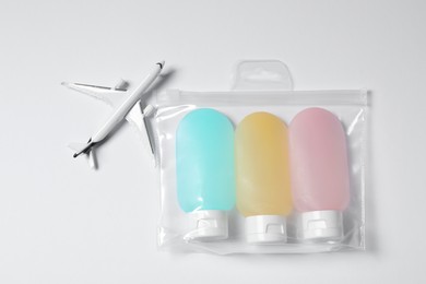 Cosmetic travel kit in plastic bag and toy plane on white background, top view. Bath accessories