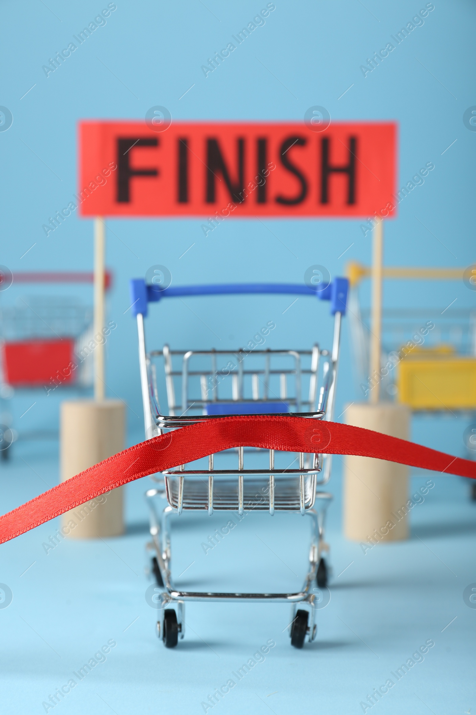 Photo of Shopping cart at red finish line on light blue background. Competition concept