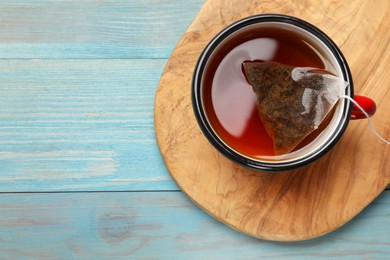 Tea bag in cup with hot drink on light blue wooden table, top view. Space for text