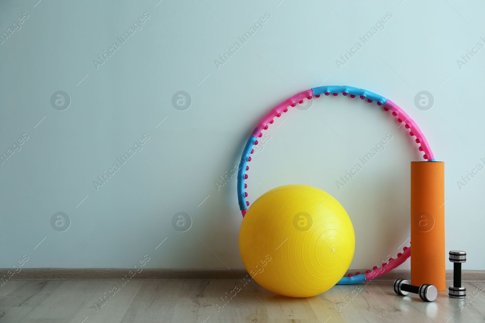 Photo of Hula hoop, fitness ball, mat and dumbbells near light wall in gym. Space for text